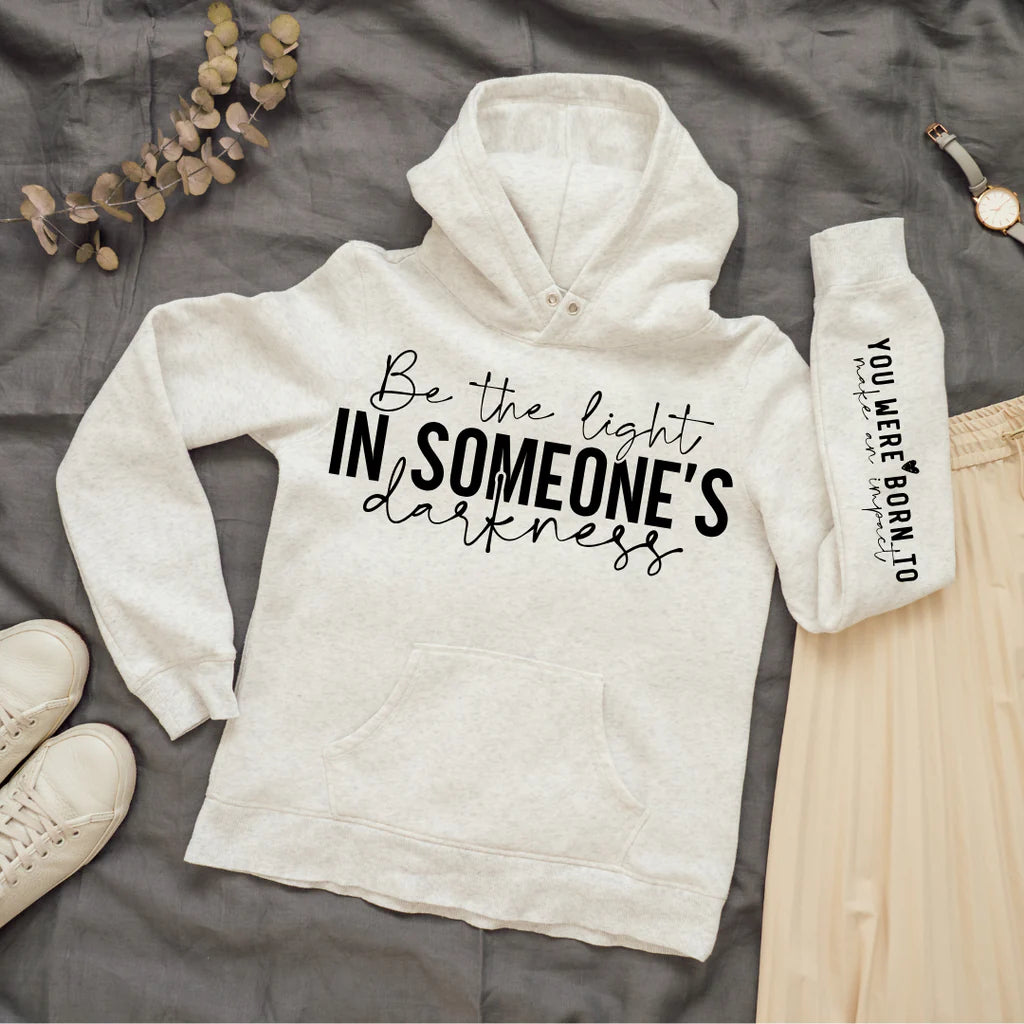 Light gray cotton blend hoodie with the inspirational message "Be the Light in Someone's Darkness" on the chest and "You Were Born to Make an Impact" on the sleeve, paired with casual and cozy accessories.