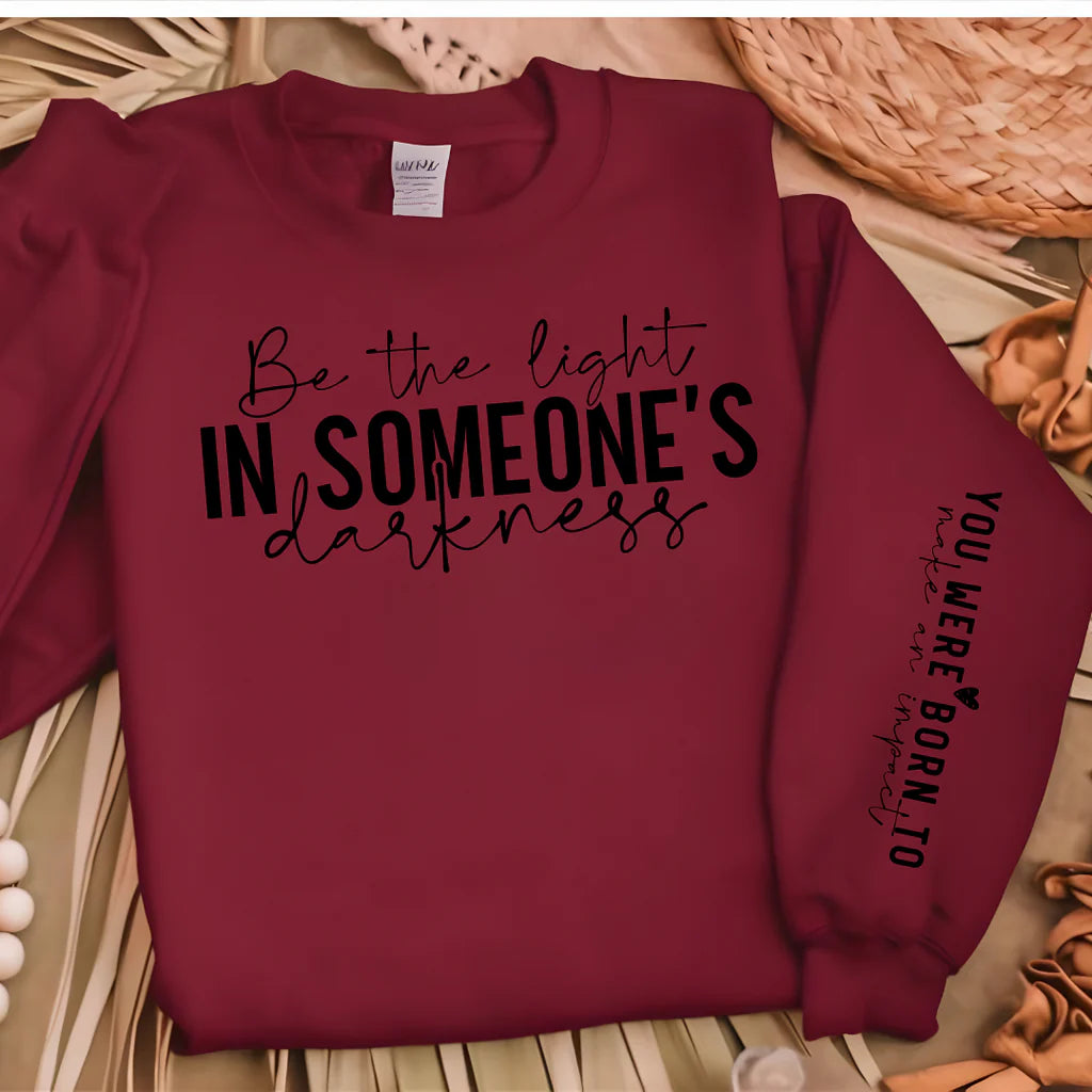 Maroon cotton blend sweater with the inspirational message "Be the Light in Someone's Darkness" on the chest and "You Were Born to Make an Impact" on the sleeve, paired with casual and cozy accessories.