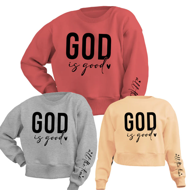 Red cotton blend sweater, gray cotton blend sweater, and pink cotton blend sweatshirt featuring the bold text "God is Good" in black on the chest and "All the Time" written on the sleeve, styled with a neutral background and cozy accents.